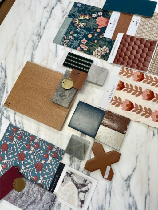 Terri Brien Interiors Material Presentation for a Dana PPoint home renovation featuring blue and red wallpaper with floral design, red and black marble sample, white oak wood floor sample, deep blue clay tile, deep maroon and cream tile, creamy and pink floral fabric, brass finish samples and various textiles